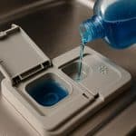 Close-up of dishwasher rinse aid dispenser compartment inside an open dishwasher appliance